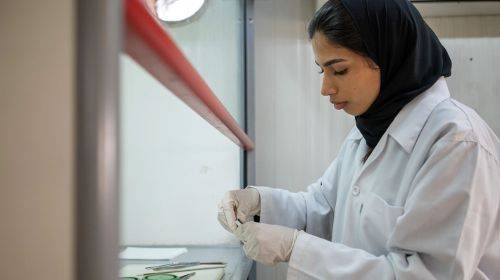 A woman wearing a lab coat conducting research, with tongs and test tubes present. 