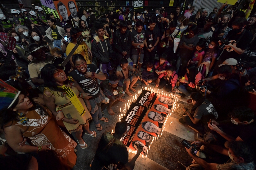 People surround a poster of two men surrounded candles